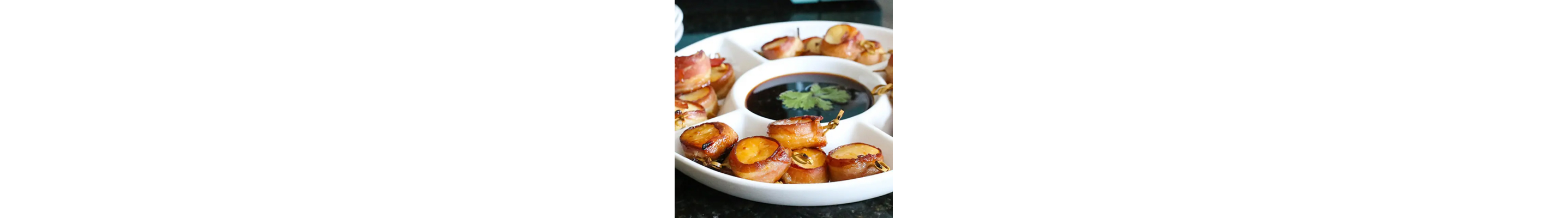 Bacon-wrapped scallops on a platter with sauce in the middle